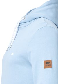 Sudadera de color azul claro hecha de una mezcla de algodón, con un bolsillo canguro, cordones blancos y una etiqueta de cuero en la manga izquierda.