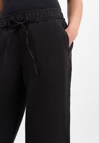 Black linen pants with an elastic waistband and drawstring, featuring side pockets and a loose, straight-leg design.