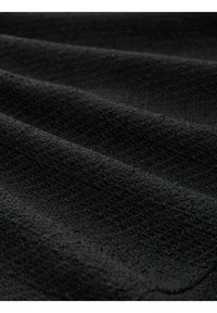 Tela negra texturizada con una apariencia suave y tejida, presenta sutiles ondas y profundidad, adecuada para ropa o tapicería.