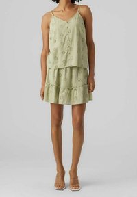 Ljusgrön klänning med ett lagerdesign, som har blommiga utskärningar och tunna axelremmar. Slät textur med en lagerkant.