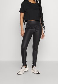 Svart kortärmad t-shirt i kombination med åtsittande svarta leggings. Leggings har sidokant. Modellen har på sig vita och grå sportskor.