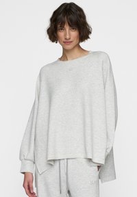 Felpa oversize grigia chiara con collo a barca, maniche lunghe a palloncino e un discreto logo centrale sul davanti. Texture del tessuto morbida.