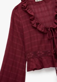 Geroezelde bordeaux blouse met lange mouwen, voorzien van een gestructureerd rasterpatroon en een kanten rand langs de zoom en de halslijn met strikdetails.