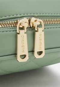 Green quilted material handbag featuring gold hardware and dual zipper pulls with engraved "Valentino" branding. Smooth texture and structured design.