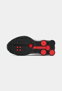 Sola de sapatilha Nike Shox preta e vermelha mostrando as distintas cápsulas de amortecimento circulares e um padrão de aderência texturizado.