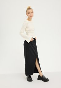 Lange zwarte spijkerrok met een split aan de voorkant, gecombineerd met een aansluitend geribd crème kleurig topje met lange mouwen. Zwarte chunky schoenen maken de look af.