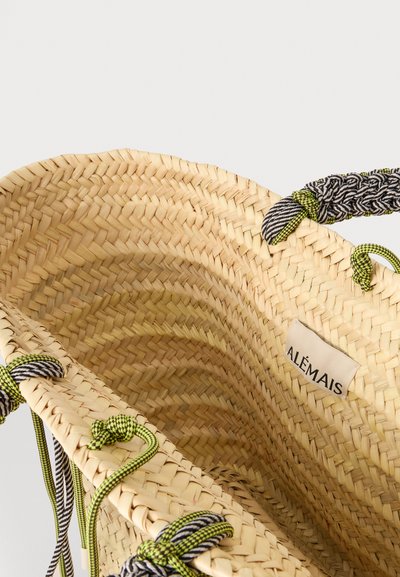 Gros plan d'un sac en paille tressée avec des anses en corde tressée noire et verte et une étiquette blanche portant la mention « ALÉMAIS » à l'intérieur.