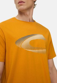 Kortærmet orange t-shirt i bomuld med et sølvfarvet grafisk design med skrå linjer over brystet.