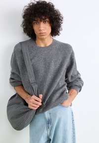 Maglione di lana grigio con scollatura tonda, vestibilità rilassata e spalle basse. Indossato con jeans in denim azzurro chiaro e una borsa a quadri grigia.