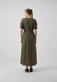 Olive roheline maxi kleit lühikeste volangkäistega, pigistatud taljega ja pehme tekstuuriga. Kantud mustade plokk-kontsadega sandaalidega.