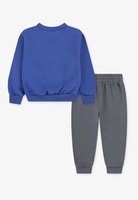 Sweatshirt azul com punhos e bainha canelados, combinado com calças de treino cinzas com cinto elástico e pernas ajustadas.