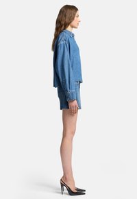 Giacca di jeans con maniche lunghe e un design cropped, abbinata a pantaloni shorts di jeans. Scarpe nere con tacco alto completano il look.