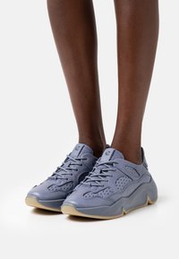 Jasnoszare sneakersy z teksturowaną cholewką, perforacjami zapewniającymi przewiewność oraz masywną, lekką gumową podeszwą o gładkim wykończeniu.