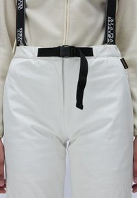 White waterproof pants with adjustable black suspenders and a black belt. The fabric has a smooth, matte texture with minimal seams.