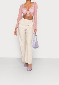 Jasnofioletowa, długorękawowa bluzka typu crop z kwiatowym wzorem, beżowe spodnie z szerokimi nogawkami, lawendowe plecione sandały oraz mała torebka o teksturze w kolorze fioletowym.