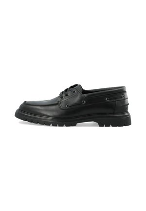 Chaussure en cuir noir avec un bout arrondi et une semelle en caoutchouc épaisse, présentant un design à lacets, des œillets en métal et des accents sur les panneaux latéraux.