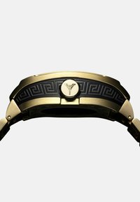 Goudkleurig horloge met een zwarte rubberen band met een Grieks sleutelpatter en een centraal embleem. Gladde textuur met gepolijste accenten.
