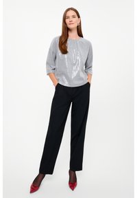 Top in paillettes argento con scollatura rotonda e maniche a tre quarti, abbinato a pantaloni neri e décolleté con punta rossa.