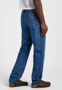 Jeans de mezclilla azul con corte recto, que presentan una etiqueta de cuero marrón en la cinturilla y dos bolsillos traseros con costuras en contraste.