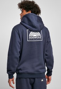 Navy blue hoodie made of soft material with a large white logo on the back, featuring a classic design and ribbed cuffs and hem.
