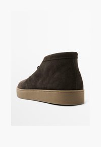 Bottines en suede marron avec un bout arrondi, un design à lacets et une semelle en caoutchouc beige contrastante. Texture lisse et détails de couture minimaux.