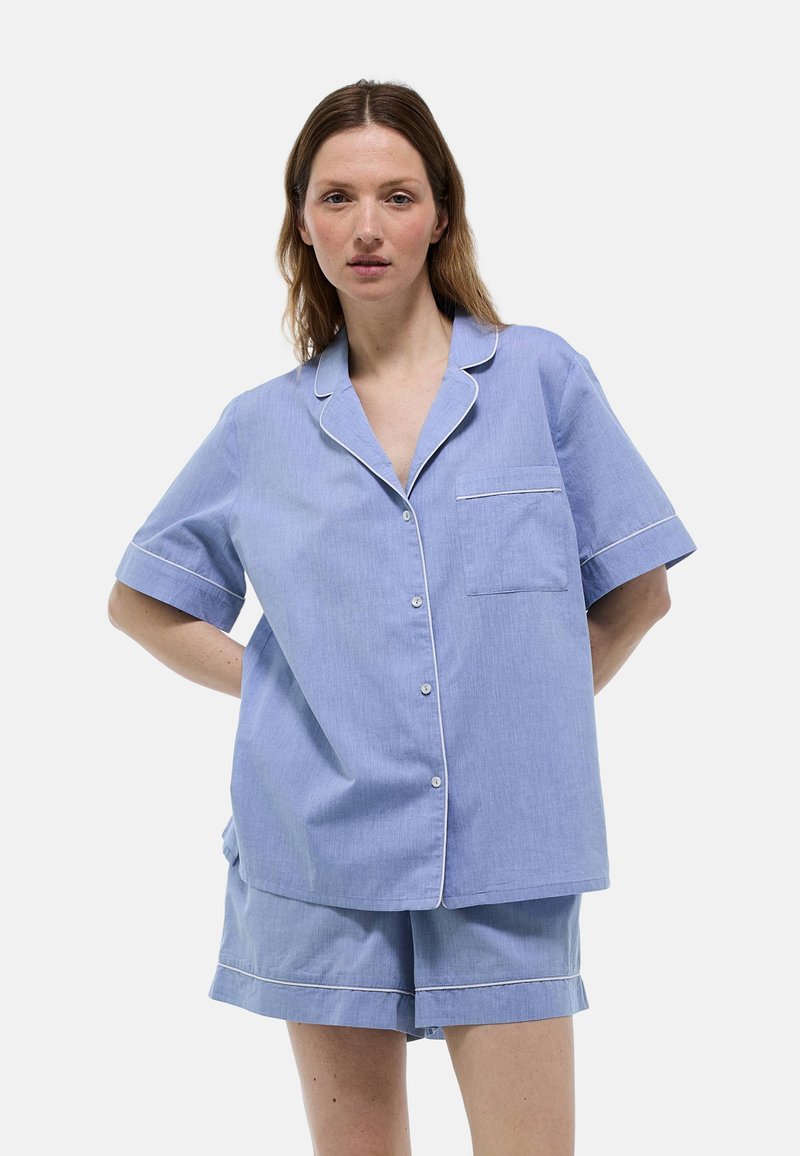 Ensemble de pyjama en coton bleu à manches courtes avec un passepoil blanc, comprenant une chemise à boutons et un short assorti avec une poche sur la chemise.
