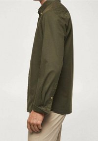 Camisa de manga larga color verde oliva con cuello, de corte holgado y botones en tono dorado en los puños y la tapeta frontal.