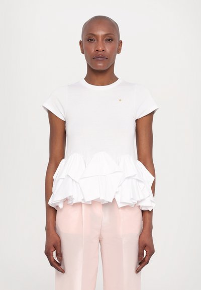T-shirt en coton blanc avec un ourlet volanté, des manches courtes, un col rond et une petite touche dorée. Associé à un pantalon brillant rose clair.