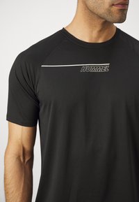 Zwarte sportieve t-shirt met korte mouwen, voorzien van een witte horizontale streep en het "HUMMEL" logo. Gemaakt van geribbelde, vochtregulerende stof.
