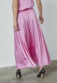 Lyserød satin maxi-nederdel med hvide prikker, elastisk talje og flydende design, sat sammen med sorte højhælede sko.