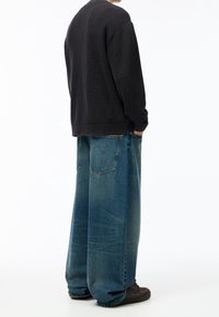 Suéter negro de punto acanalado con un corte relajado, combinado con unos vaqueros de denim azul de pierna ancha con un acabado deslavado y dos bolsillos traseros.