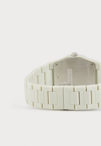 Une montre vert clair avec un bracelet en silicone présentant des maillons rectangulaires et un fond en acier inoxydable argenté. Design minimaliste, texture solide.