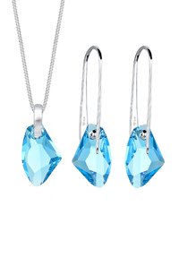 Ensemble de collier pendant et de boucles d'oreilles comprenant des cristaux taillés bleu clair, des chaînes en métal argenté et un design minimaliste avec des formes angulaires.
