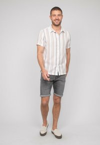 Chemise à manches courtes, à boutons, avec des rayures verticales beige clair et blanches, associée à un short en denim gris et des chaussures légères à enfiler.