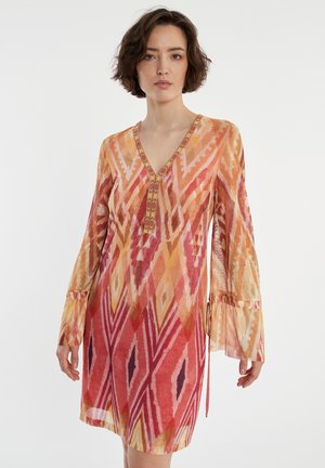 Robe à manches longues en tissu léger, avec un décolleté en V, des motifs géométriques vibrants en rouge, orange et jaune, et des manches évasées.