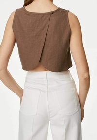 Top corto de lino marrón con un espalda con borde festoneado y cierre de botones, combinado con unos vaqueros blancos de cintura alta que presentan bolsillos estándar.