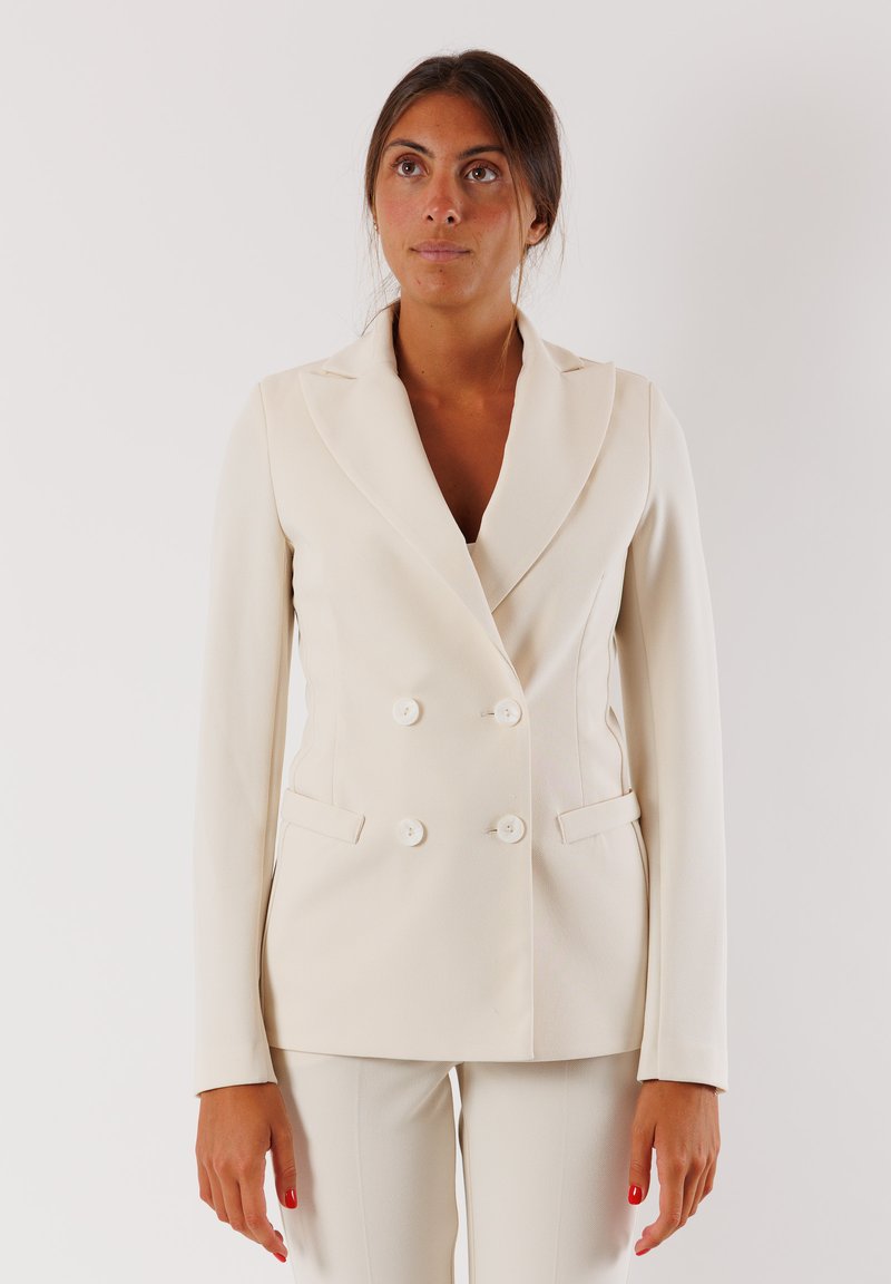 Blazer doppiopetto color crema con colletto a risvolto, due tasche frontali e chiusura con bottoni. Tessuto liscio con una forma sartoriale.