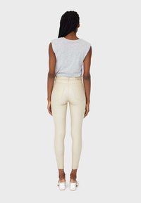 Ljust beige slim fit-jeans med hög midja, med minimala sömnadsdetaljer, i kombination med en grå ärmlös topp. Enkel bakgrund.