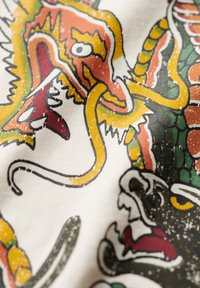 Ilustración de un dragón en tela, con colores vibrantes como naranja, verde y amarillo, con líneas y patrones texturizados en un diseño audaz.