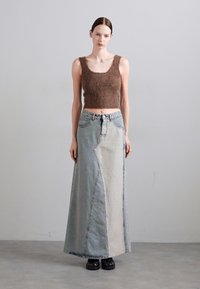 Brūns pūkains crop tops, kas savienots ar garu džinsi svārku ar dažādu toņu zilās un pelēkās krāsas panelēm. Melni platformas apavi.