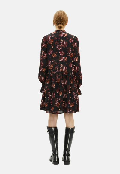 Schwarzes Kleid mit floralem Muster in Burgunder- und Orangetönen, mit langen Ärmeln, gestuftem Saum, kombiniert mit knielangen schwarzen Stiefeln.