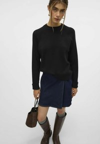 Črn pulover z raglan rokavi, v kombinaciji z denim krilom. Rjava visoka čevlja in mala rjava torbica dopolnjujeta oblačilo.