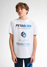 Tricou alb din bumbac cu text negru și albastru. Prezintă logo-ul "PETROLIND", "Miami Beach" și "Florida U.S.A." imprimate în dimensiuni diverse.