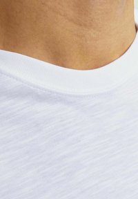 Hvid crew neck t-shirt med tekstureret stof, glat overflade og strækbar ribkant. Nærbillede af detaljerne ved halsudskæringen.
