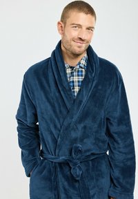 Robe en polaire bleu marine avec un col châle, une taille ceinturée et des poches latérales. Sa texture douce et sa finition lisse offrent chaleur et confort.