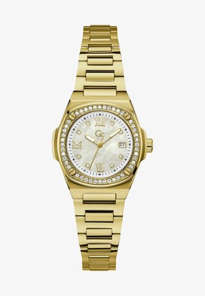 Guldfarvet metalur med en urskive i perlemor og krystal detaljer. Har et rundt ansigt, romerske talmarkører og en datovisning.