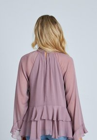 Blusa in chiffon leggero color mauve, fluente, con maniche lunghe a forma di campana e orlo arricciato. Il dettaglio a chiave sul retro aggiunge interesse al design.