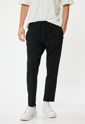 Sorte tapered bukser med elastisk talje og snor, med sidelommer, kombineret med hvide sneakers. Glat stofstruktur.