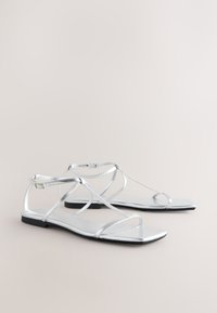 Sandalias planas plateadas con múltiples correas delgadas, puntera cuadrada, diseño elegante y suela texturizada. Hebillas ajustables que mejoran el ajuste y el soporte.
