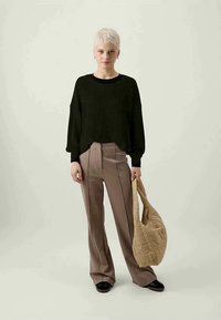 Pulover verde închis cu benzi, pantaloni bej cu croială largă și cusături laterale, și o geantă bej matlasată, având un croi relaxat și o textură netedă.